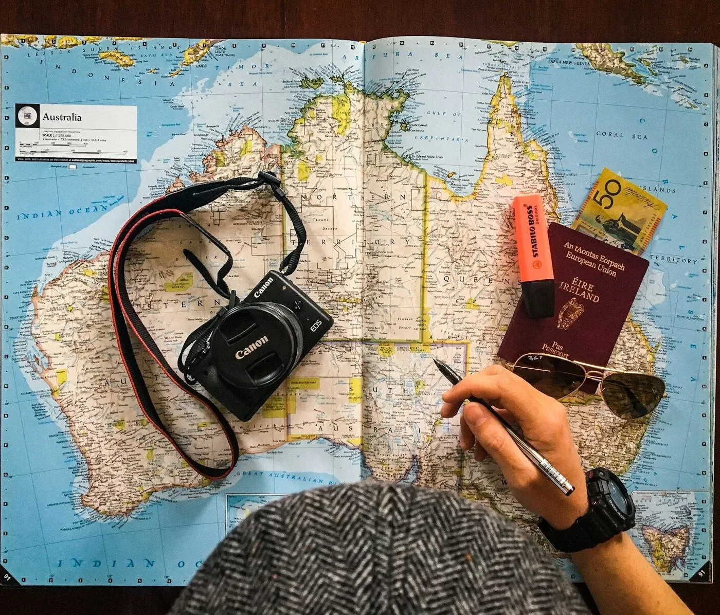 flat lay photography of person holding pen in front of world map