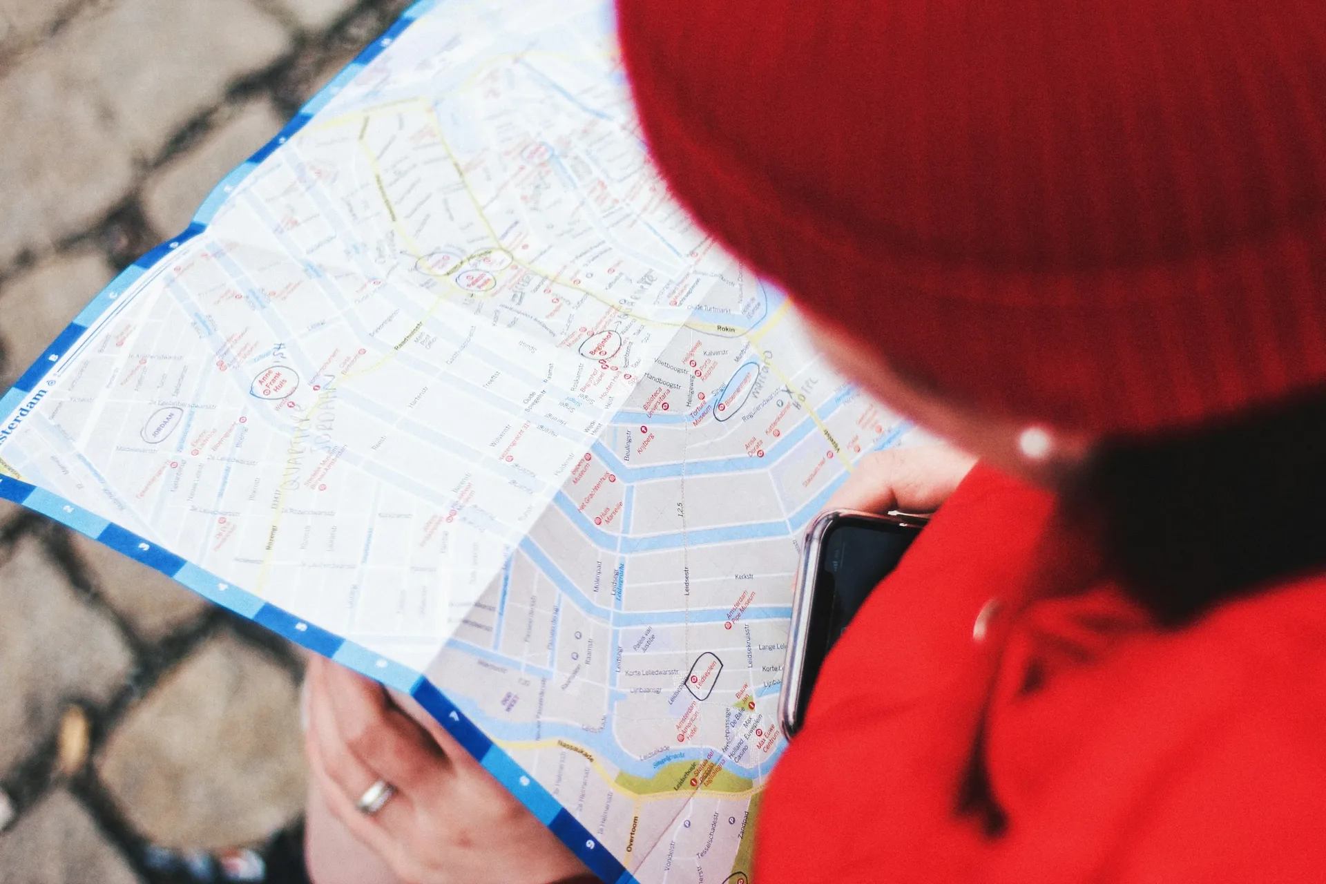 A traveler in a red hat reading a paper map, with a phone in hand
