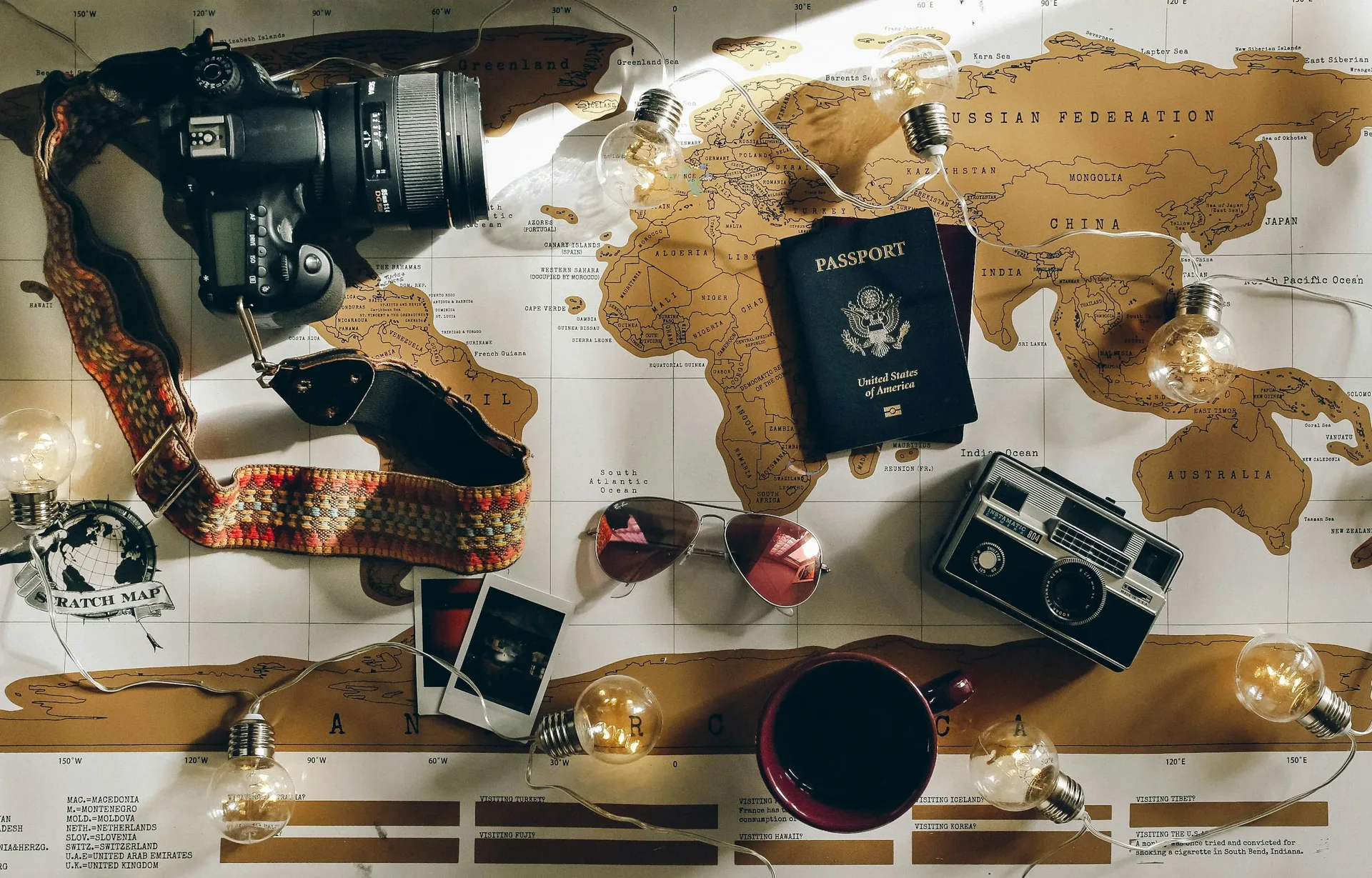A camera, a passport and instant photos laid out on a world map
